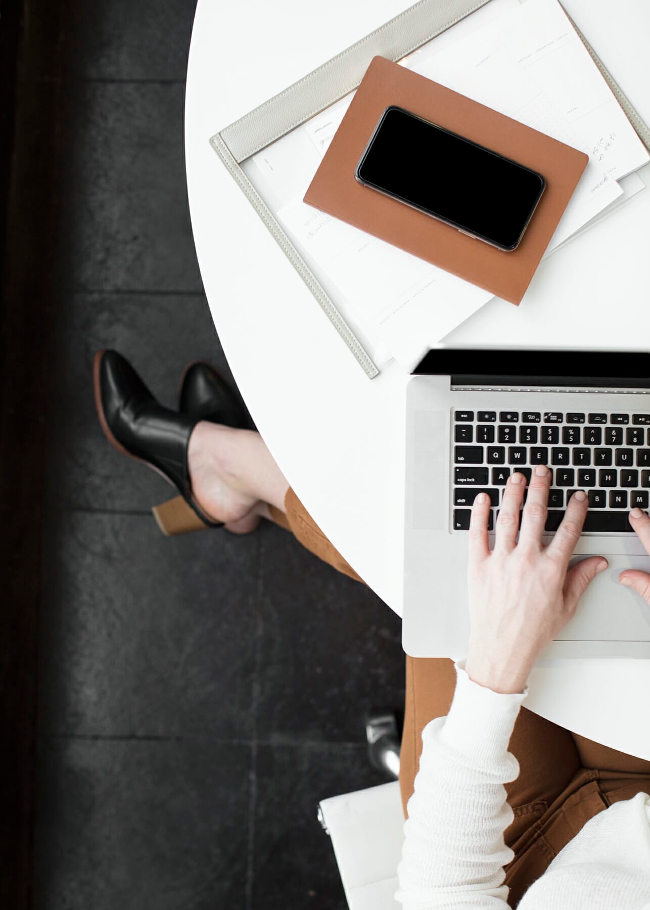 Woman with heels working on laptop with camel notebook